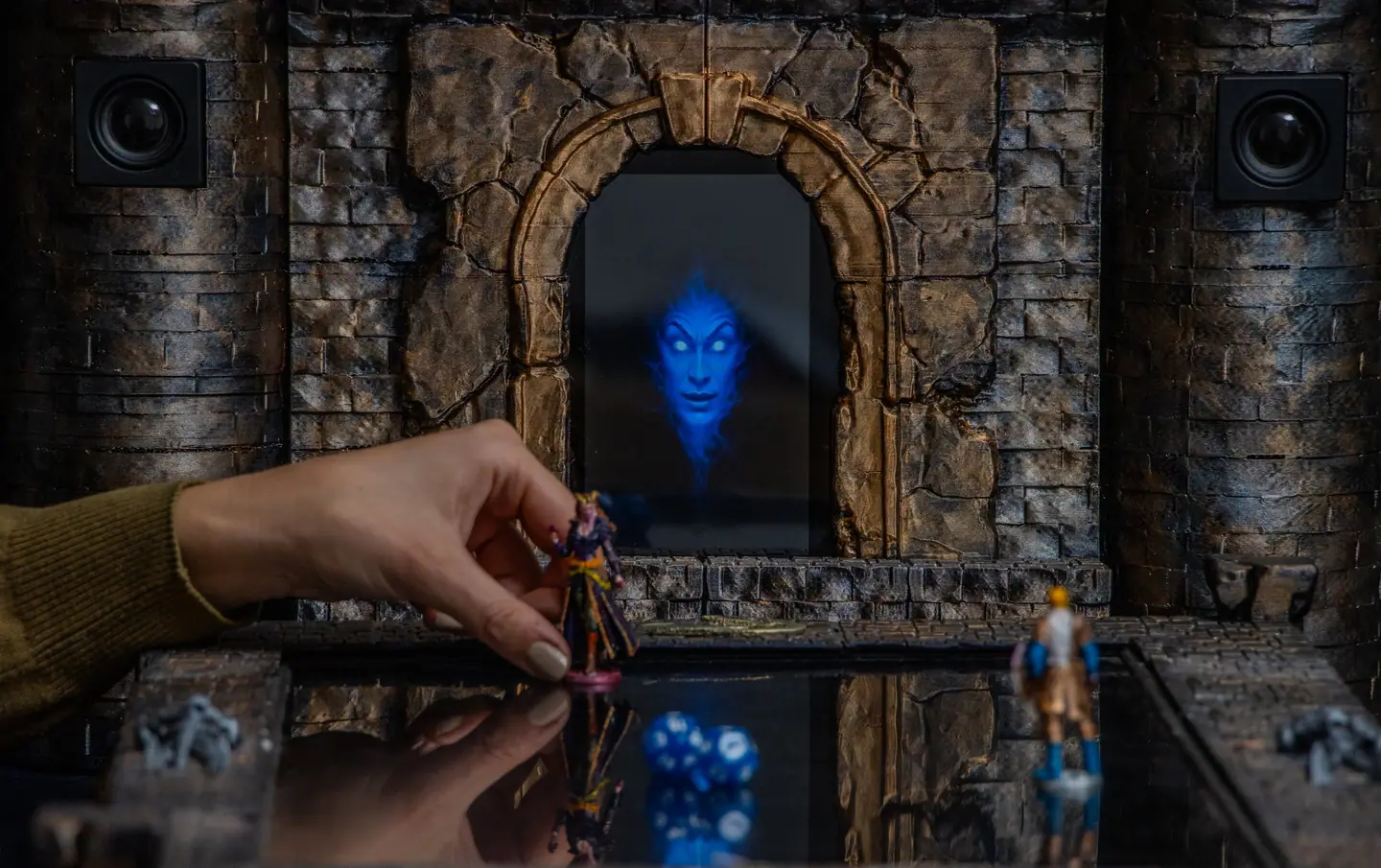 Eine Hand setzt eine Miniatur auf das Doungim Kartenbrett, über ihr ein leuchtendes Gesicht auf dem Torbildschirm