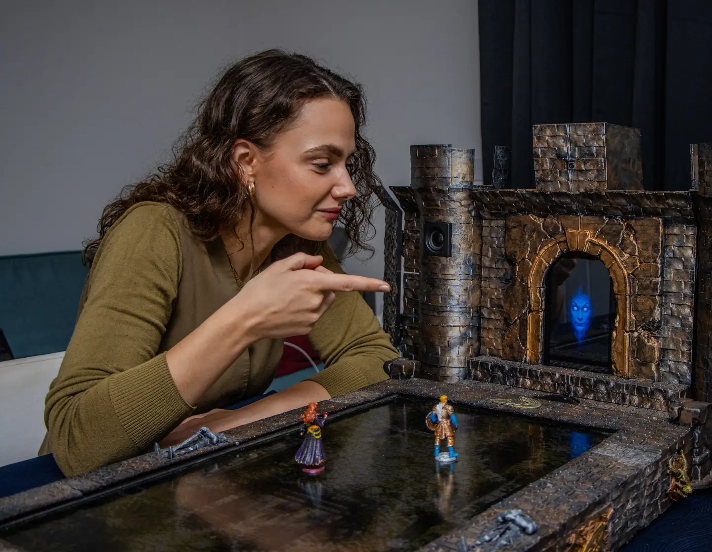 A player points at the map board while a miniature stands on it and the gate screen glows behind